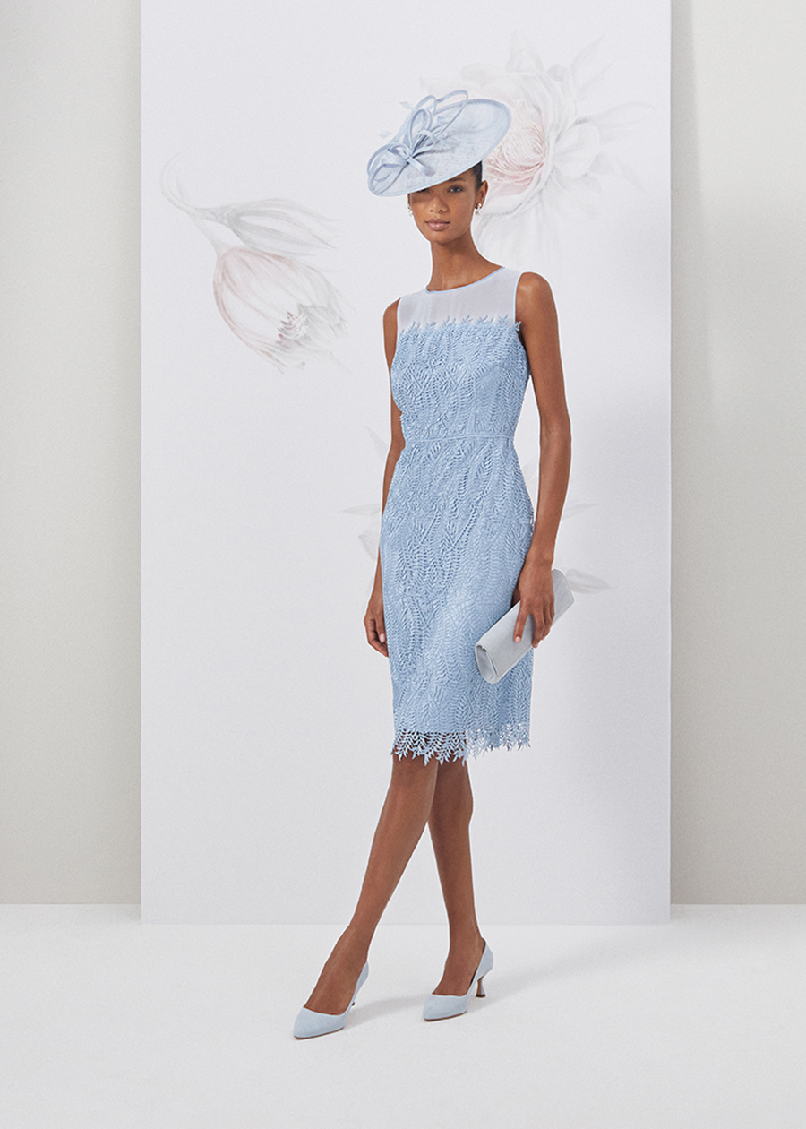 Image of model standing in front of a floral painted background wearing a pale blue lace dress with matching fascinator and accessories.
