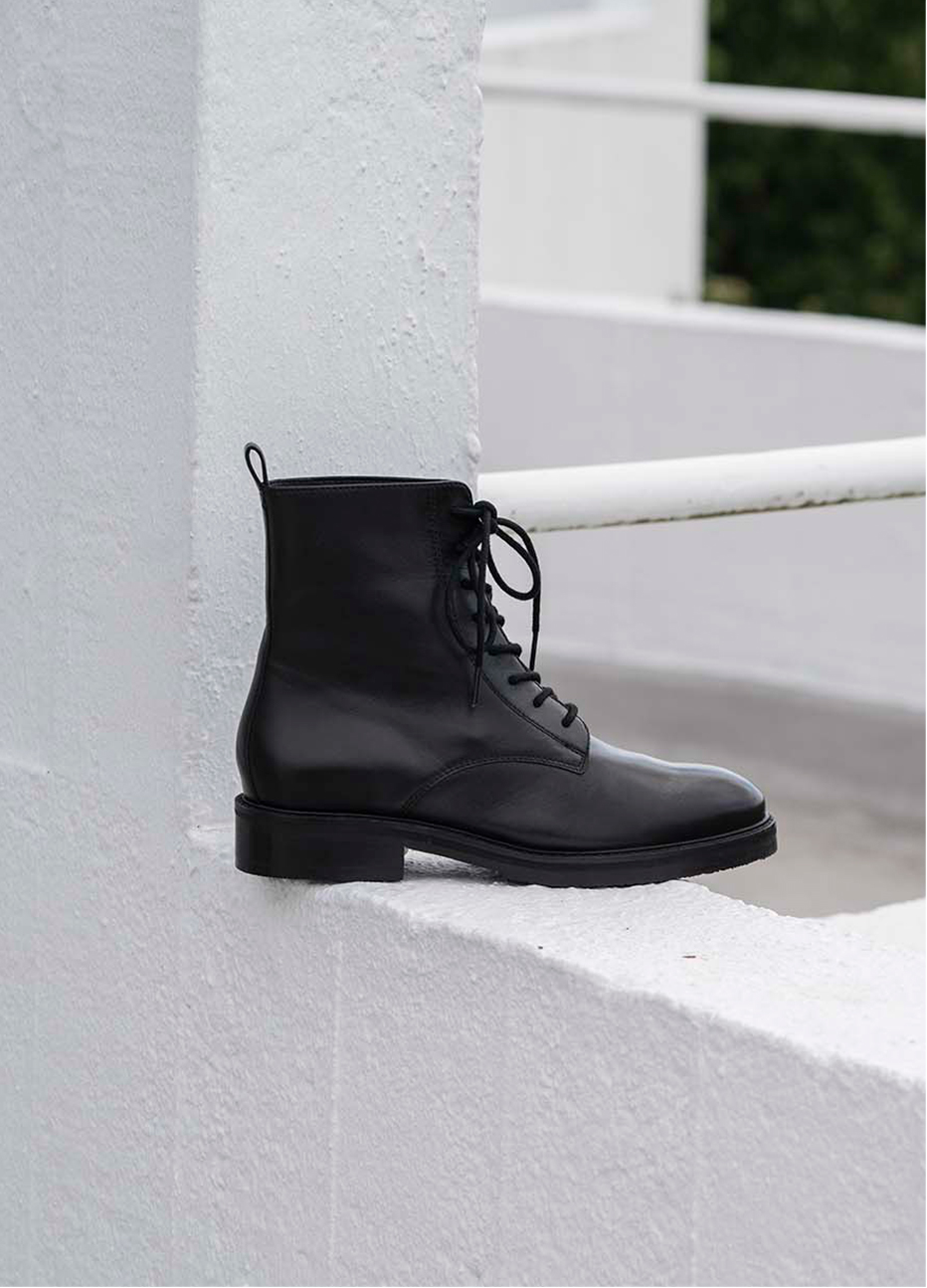 Image of a black ankle boot with buckle detail displayed on an outdoor wall.