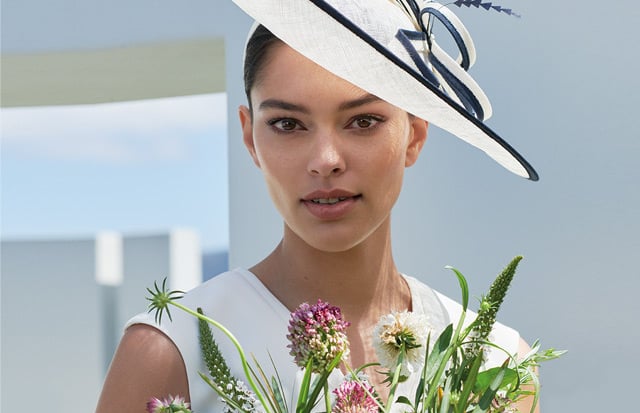 Women poses in an ivory and navy fascinator with a bunch of flowers.