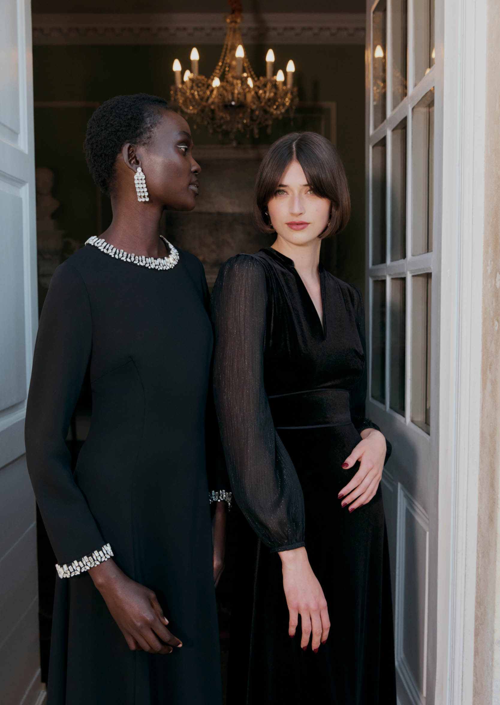 A close-up image of two models standing in a doorway wearing black occasion dresses.