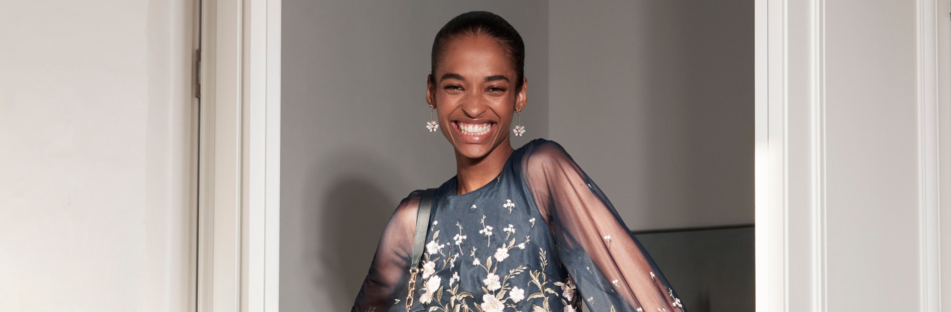 Hobbs model emerges from a room wearing a navy floral dress with matching accessories.