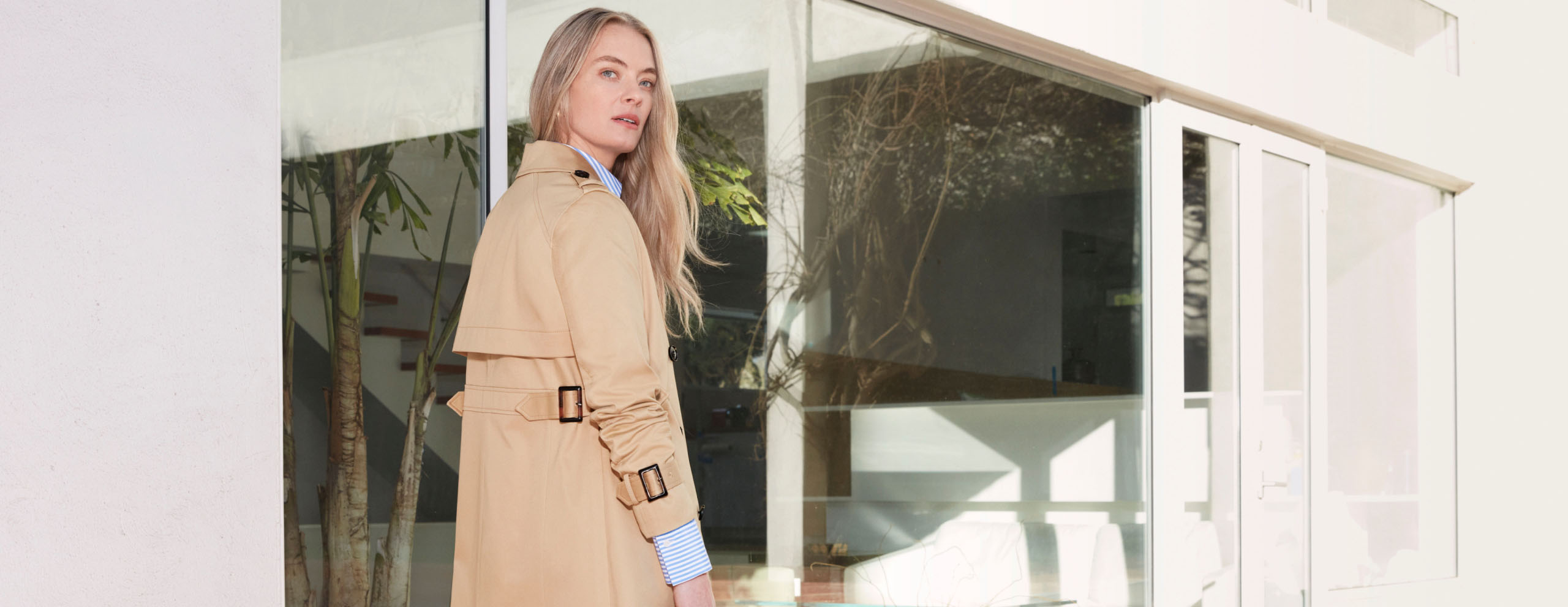 Model photographed leaning against the front door of a house wearing a cream dress suit.