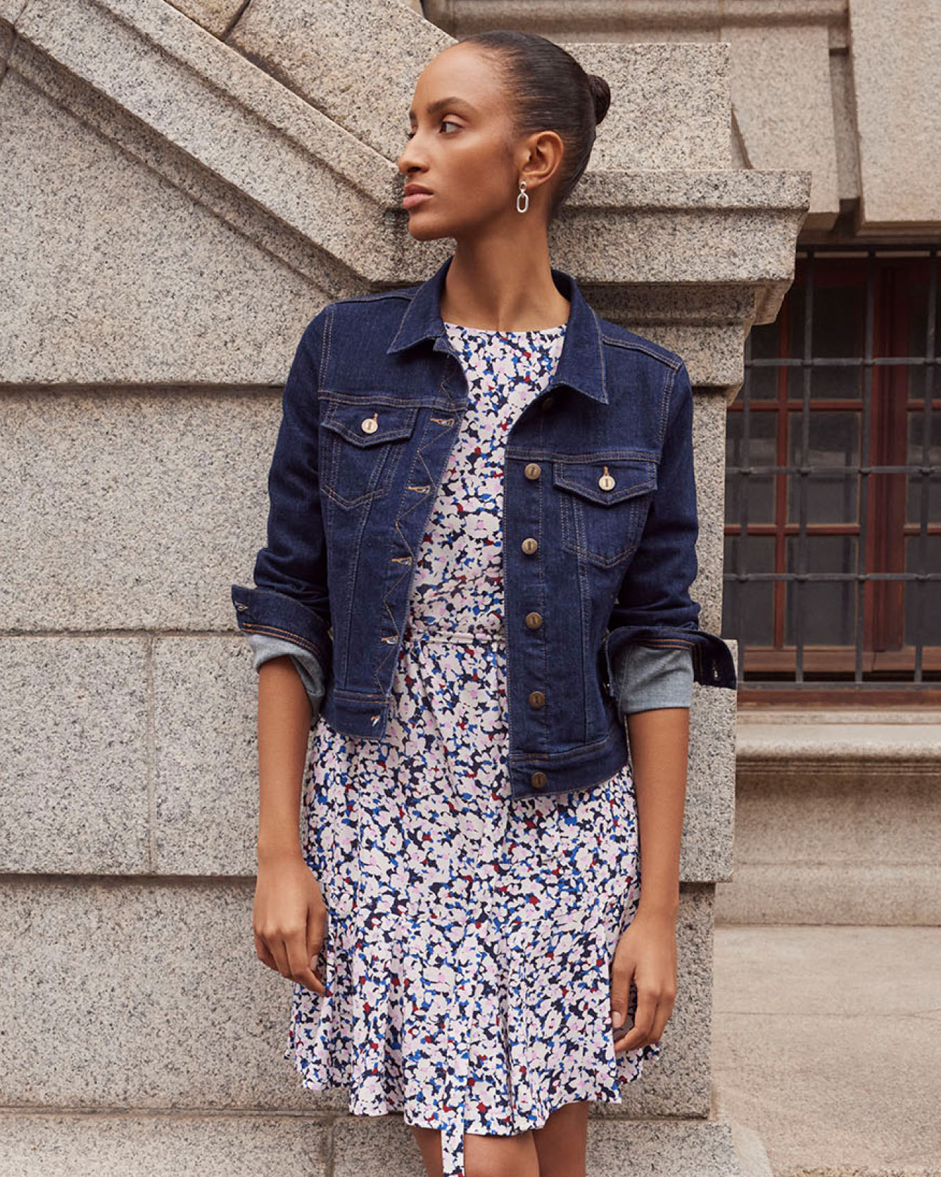 Hobbs model wears an indigo denim jacket layered over a floral dress.