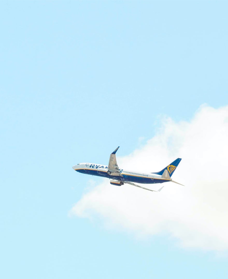 An aeroplane flys across a blue sky with a cloud