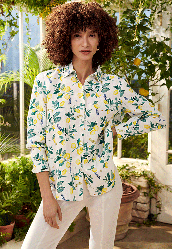 Model photographed in a conservatory wearing Hobbs lemon print linen shirt with white capri trousers.