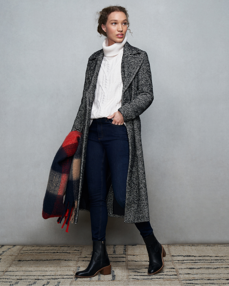 Model photographed against a canvas background wearing a Hobbs herringbone wrap coat, cable knit jumper, jeans and black ankle boots.