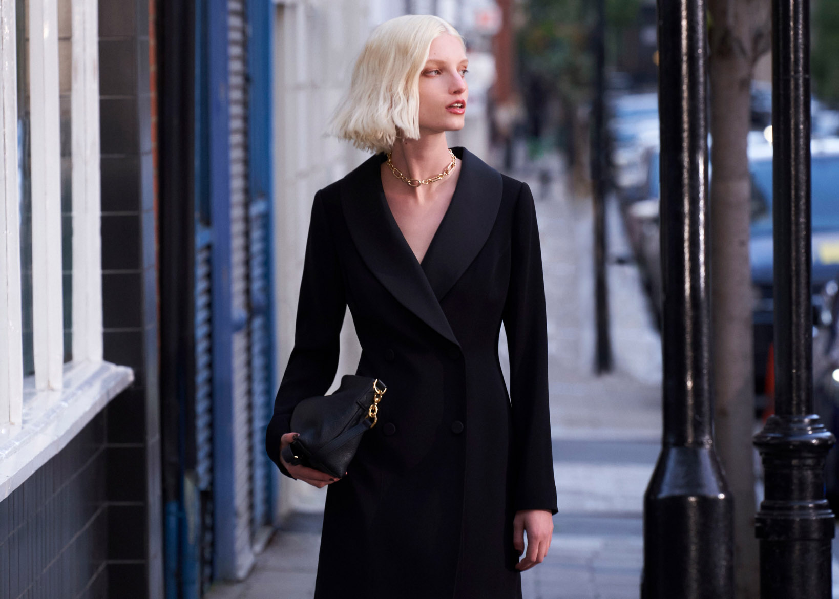 Model photographed walking down a street wearing a black tuxedo mini dress.