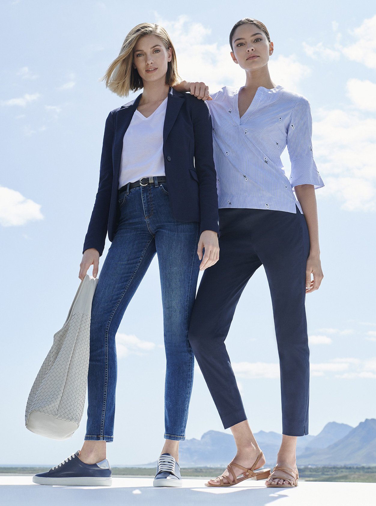 Outfit on the left features a women’s blazer in navy worn with a white t-shirt, a leather belt, blue slim fit jeans, a white leather tote bag and blue women’s trainers. Outfit on the right features a pale blue blouse with blue chinos for women and tan sandals, by Hobbs.