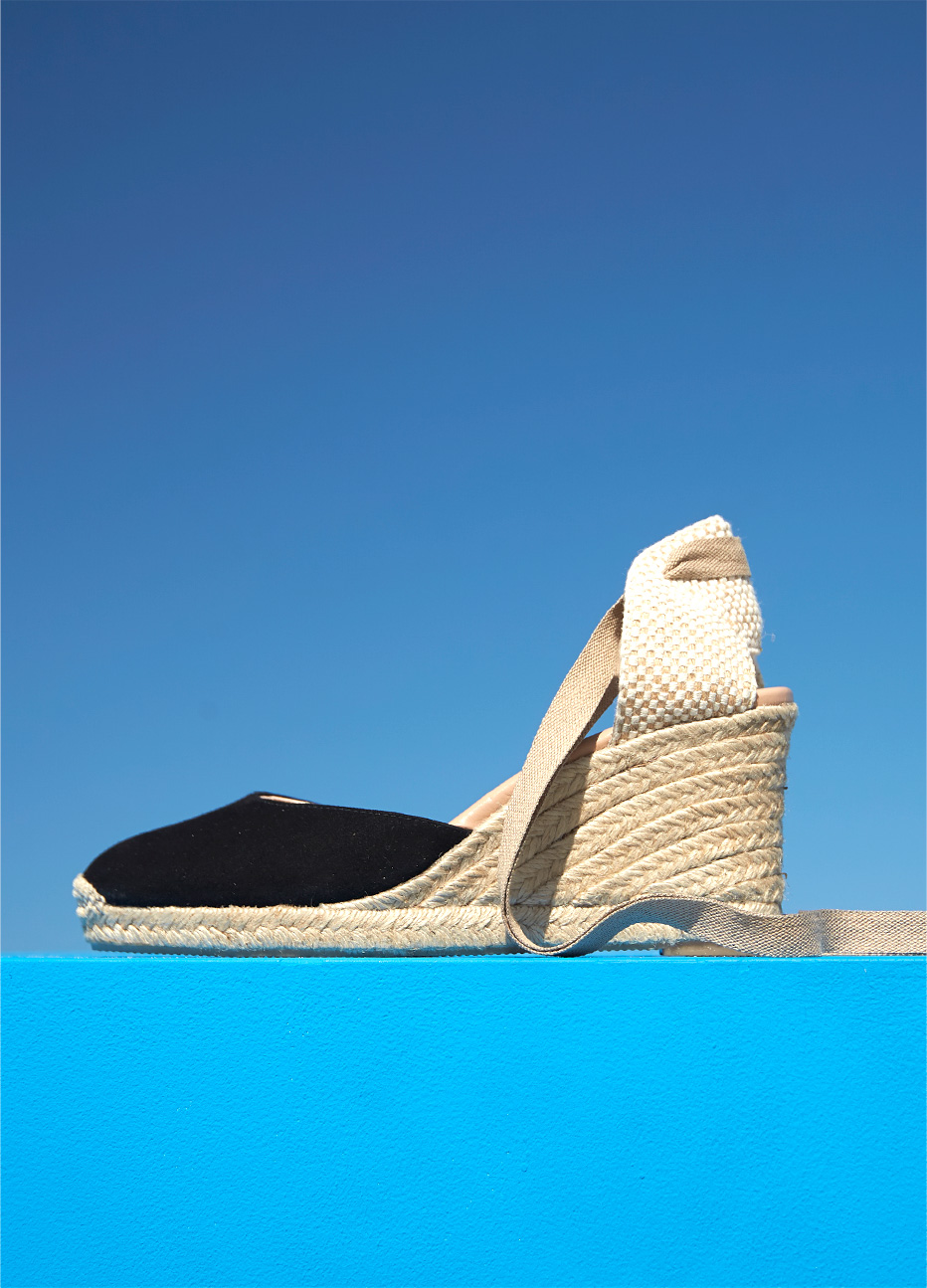 Black espadrille wedge with an ankle wrap design by Hobbs set against a blue background.