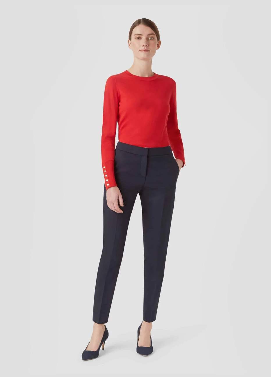 Red knitted jumper with buttons on sleeves paired with black slim fit trousers and black court shoes by Hobbs.