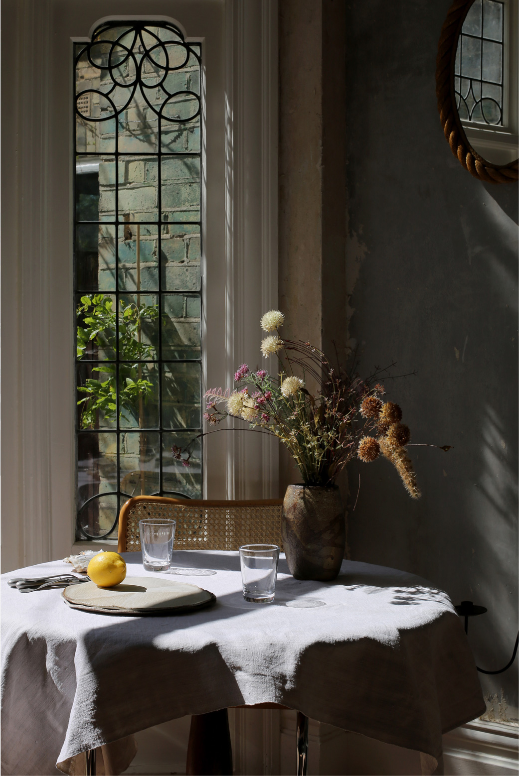 Set the table, a sundappled table is set with flowers,candles, a pale blue tablecloth. 