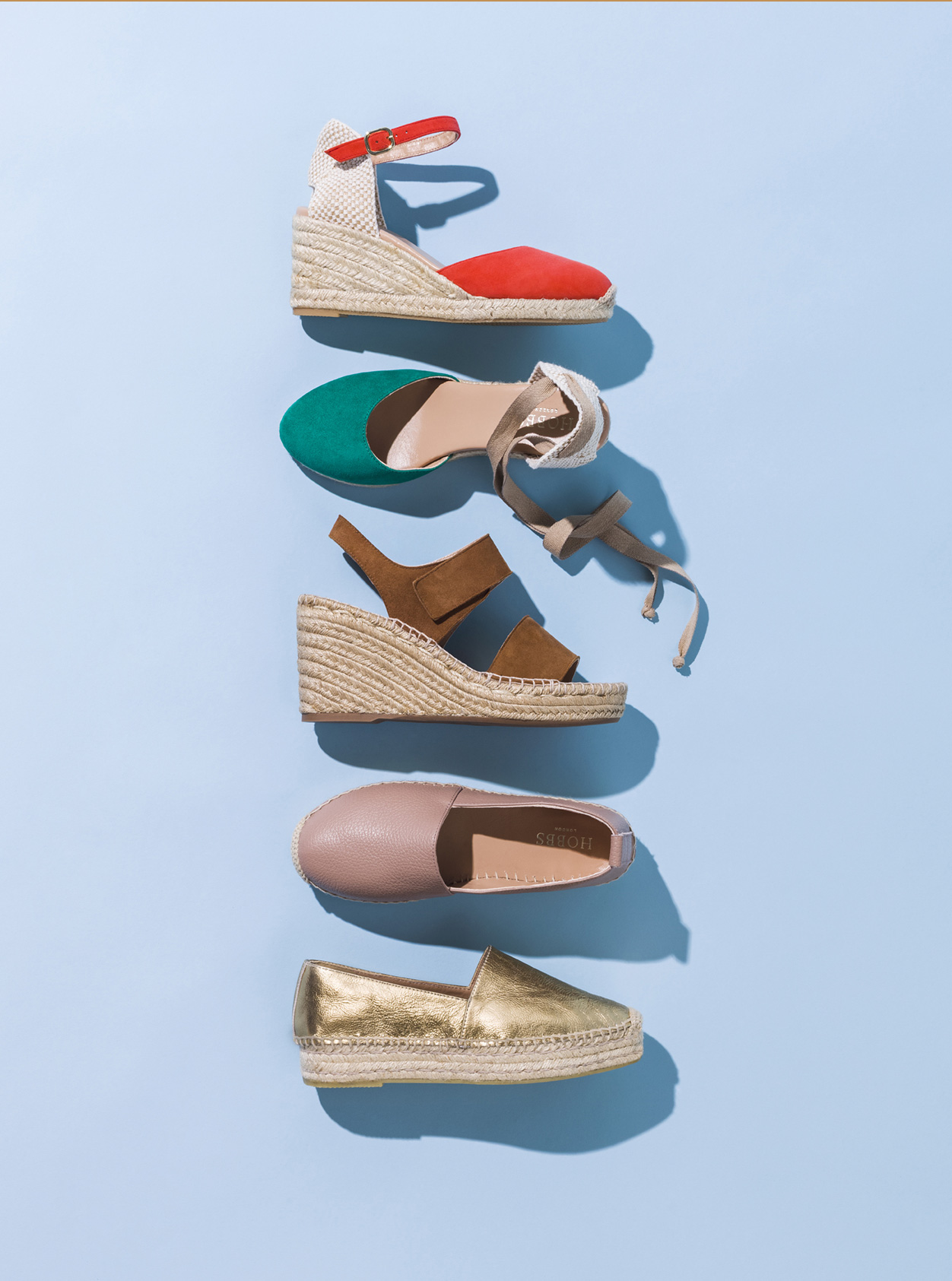 Hobbs espadrille wedges set against a blue background. From top to bottom: Red, green, brown, nude and gold.