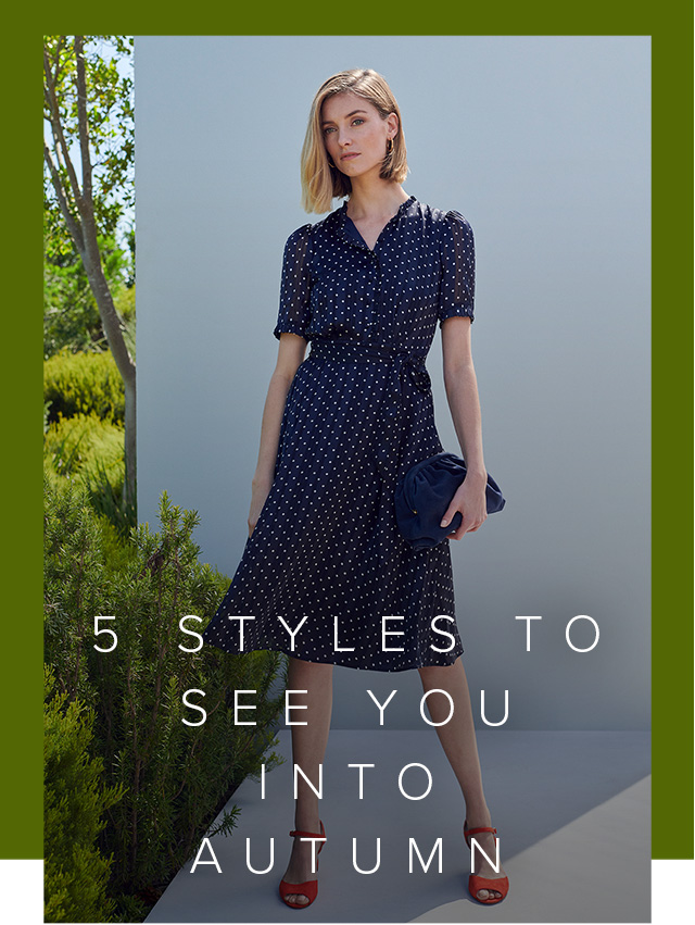 A woman poses in a navy blue and white spotty silk shirt dress with red heeled sandals. 