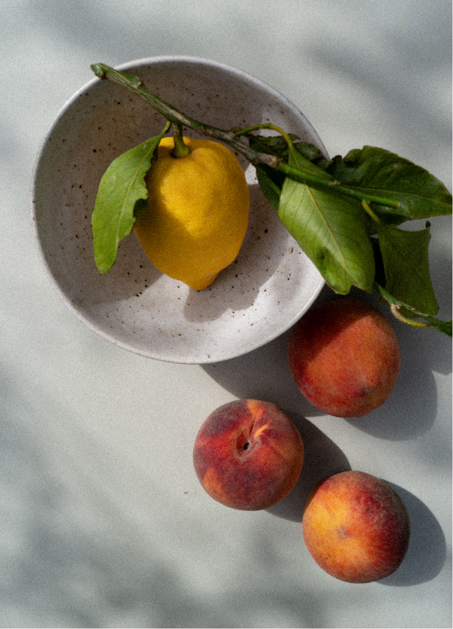 Photograph of a lemon branch in a bowl surrounded by peaches, captured by photographer Charlotte Bland.