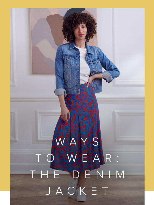 Photographed in front of contemporary abstract art, model wears a denim jacket with a white t-shirt, floral midi skirt and trainers.