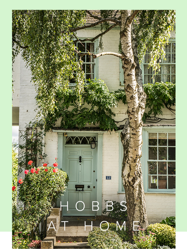 A serene pale grey green door with a picturesque pink flowers and green foliage surrounding it. 