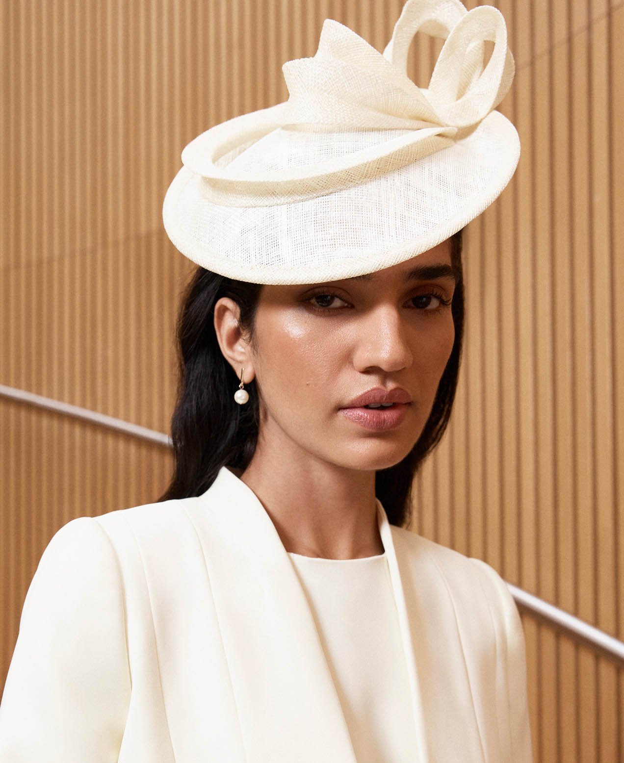 A woman wearing a butter yellow occasion outfit and coordinating fascinator.