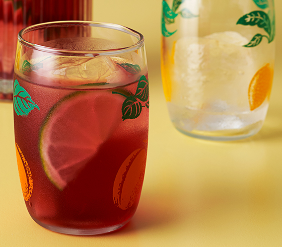 A jug of homemade lemonade, bowl of fresh lemons and a silk scarf sit atop a table.