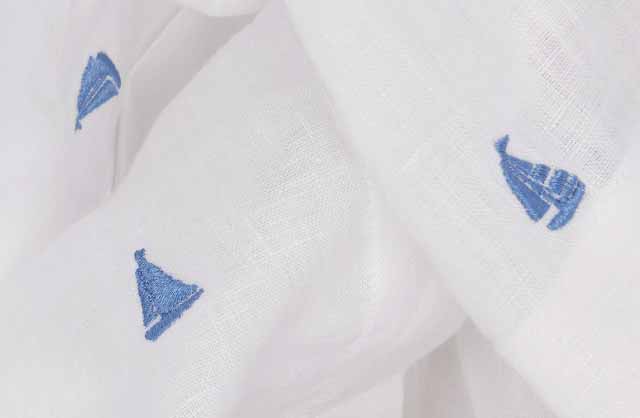 Close-up image of blue embroidered boats on white linen fabric.