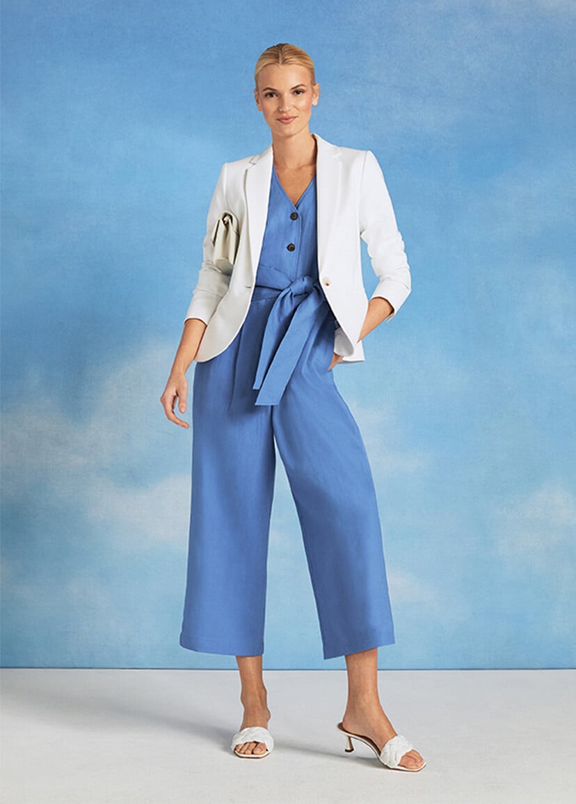 Model photographed against a sky background wearing a blue jumpsuit and white blazer.