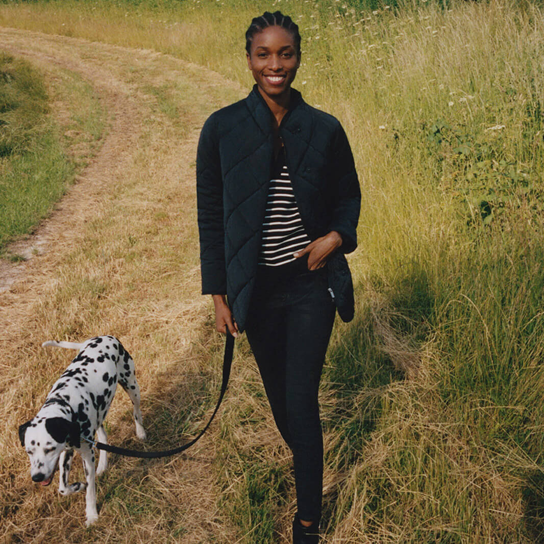 Image of model walking a Dalmation dog through a field wearing a Hobbs puffer jacket, striped jumper and jeans.