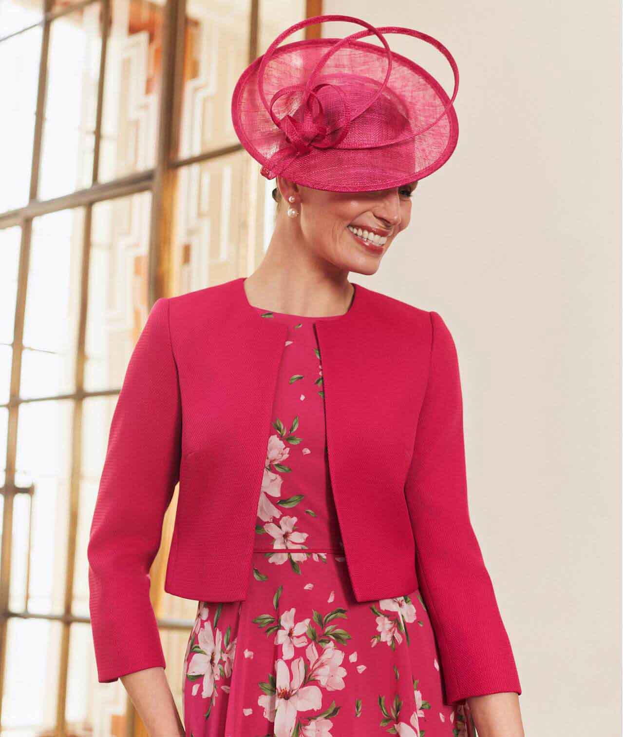 Hobbs model wears a pink floral dress with a matching fascinator and jacket.