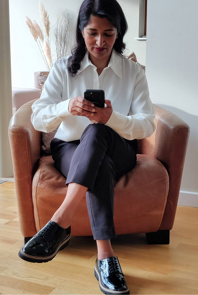 Photographed at home on her phone, fashion blogger Monika Mandal wears Hobbs Eva silk shirt, petite Quin navy trousers and Bloomsbury black patent lace-up shoes.