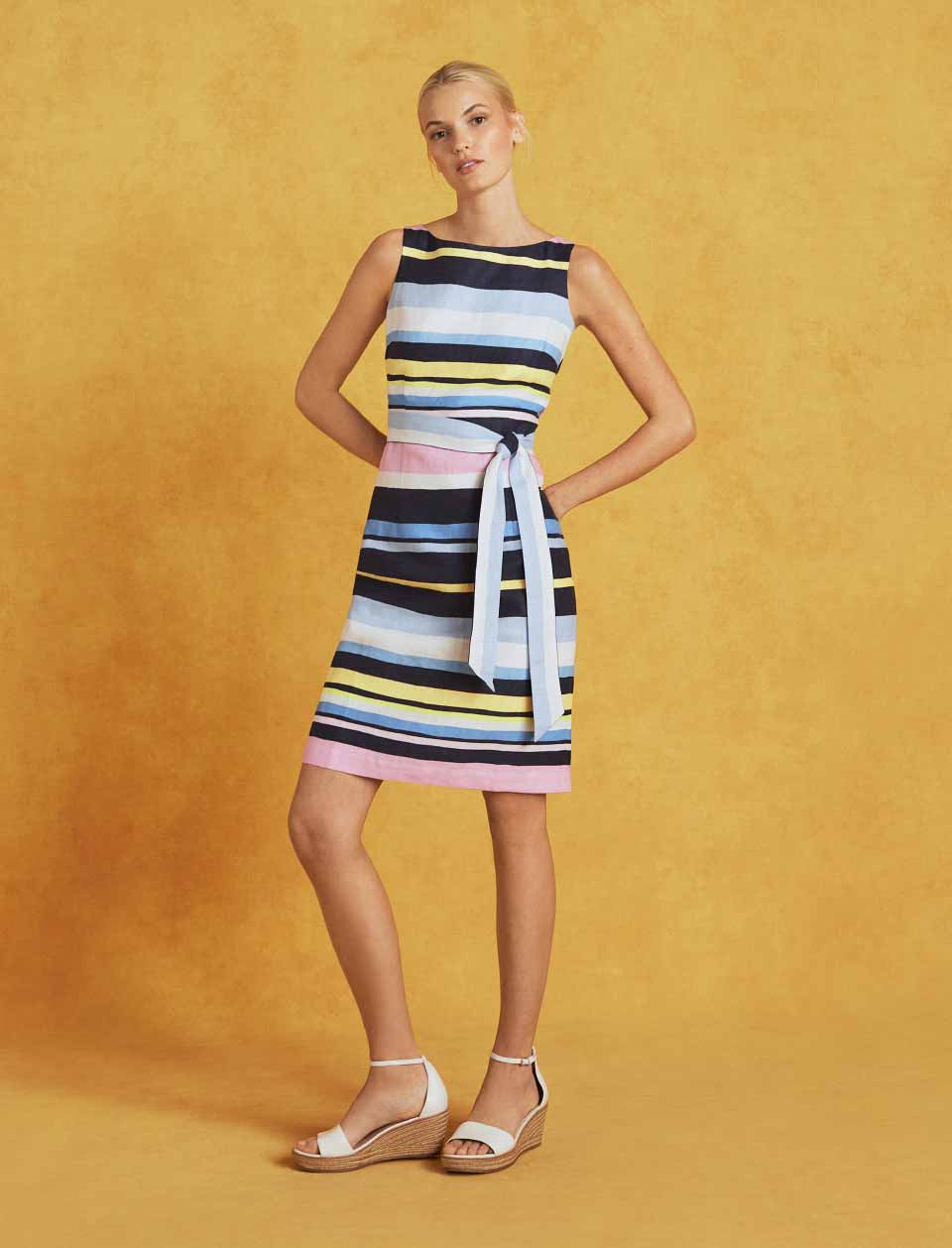 Model photographed in front of a yellow background wearing a striped linen dress.