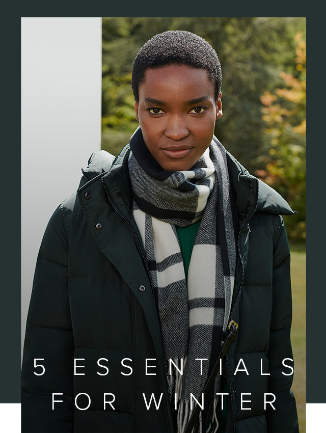 Close-up of model in a garden wearing a puffer coat and checked scarf.