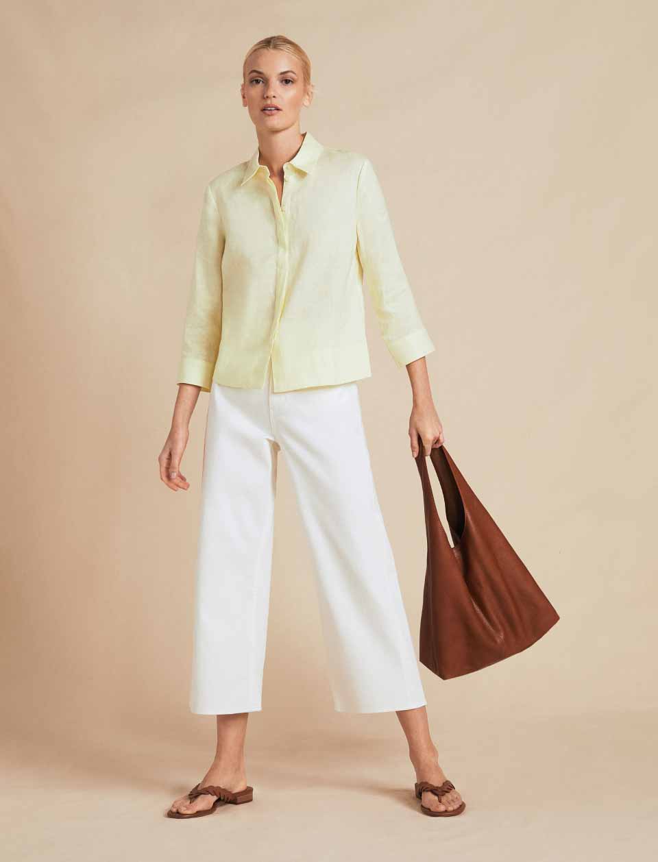 Model photographed in front of a beige background wearing a yellow linen shirt and white cropped jeans.