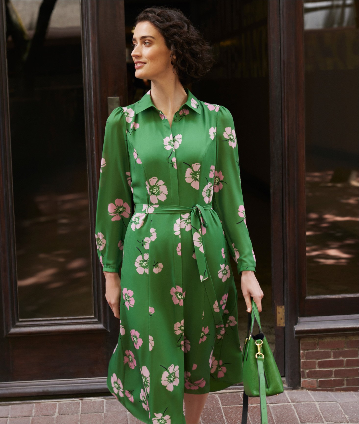 Photo of model leaving a shop wearing a green floral shirt dress.