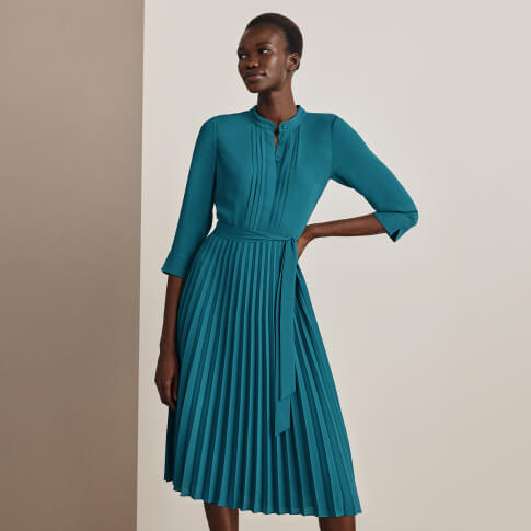 Hobbs model wears a teal midi dress with a pleated skirt.