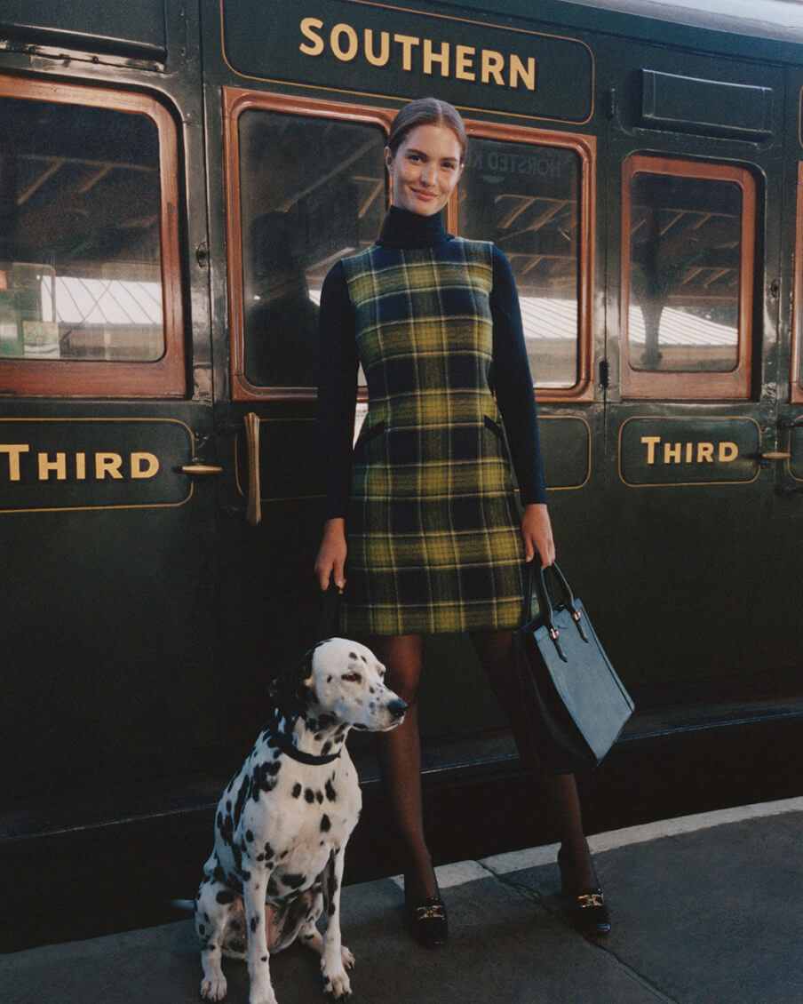 Hobbs model stands next to a heritage train with a dalmatian dog, wearing a check