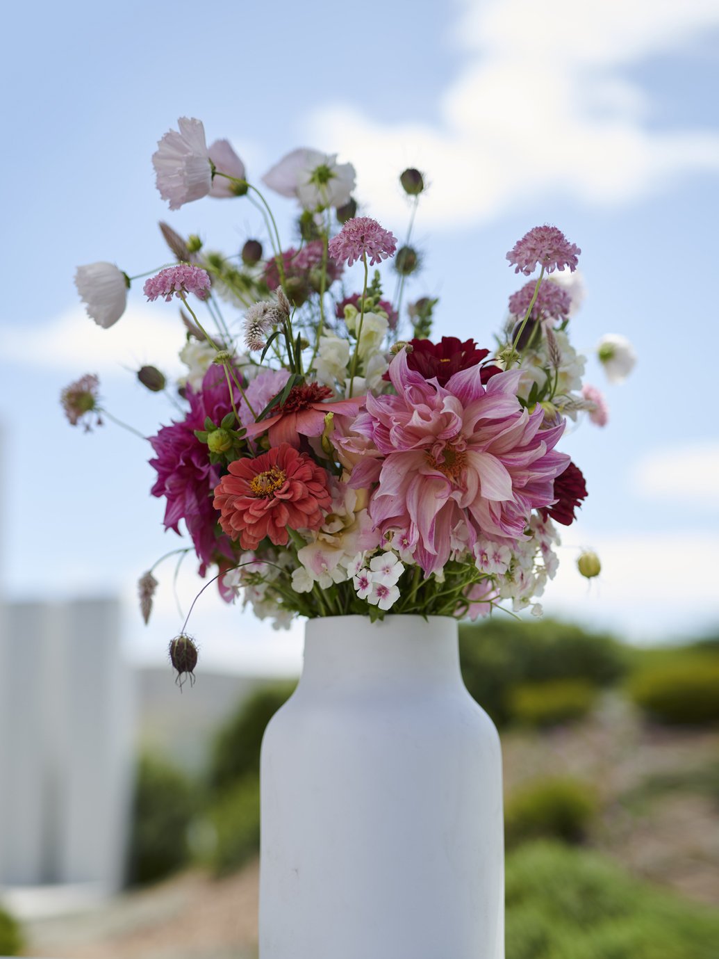 A bouquet of pink, red and white spring flowers in a white ceramic vase.