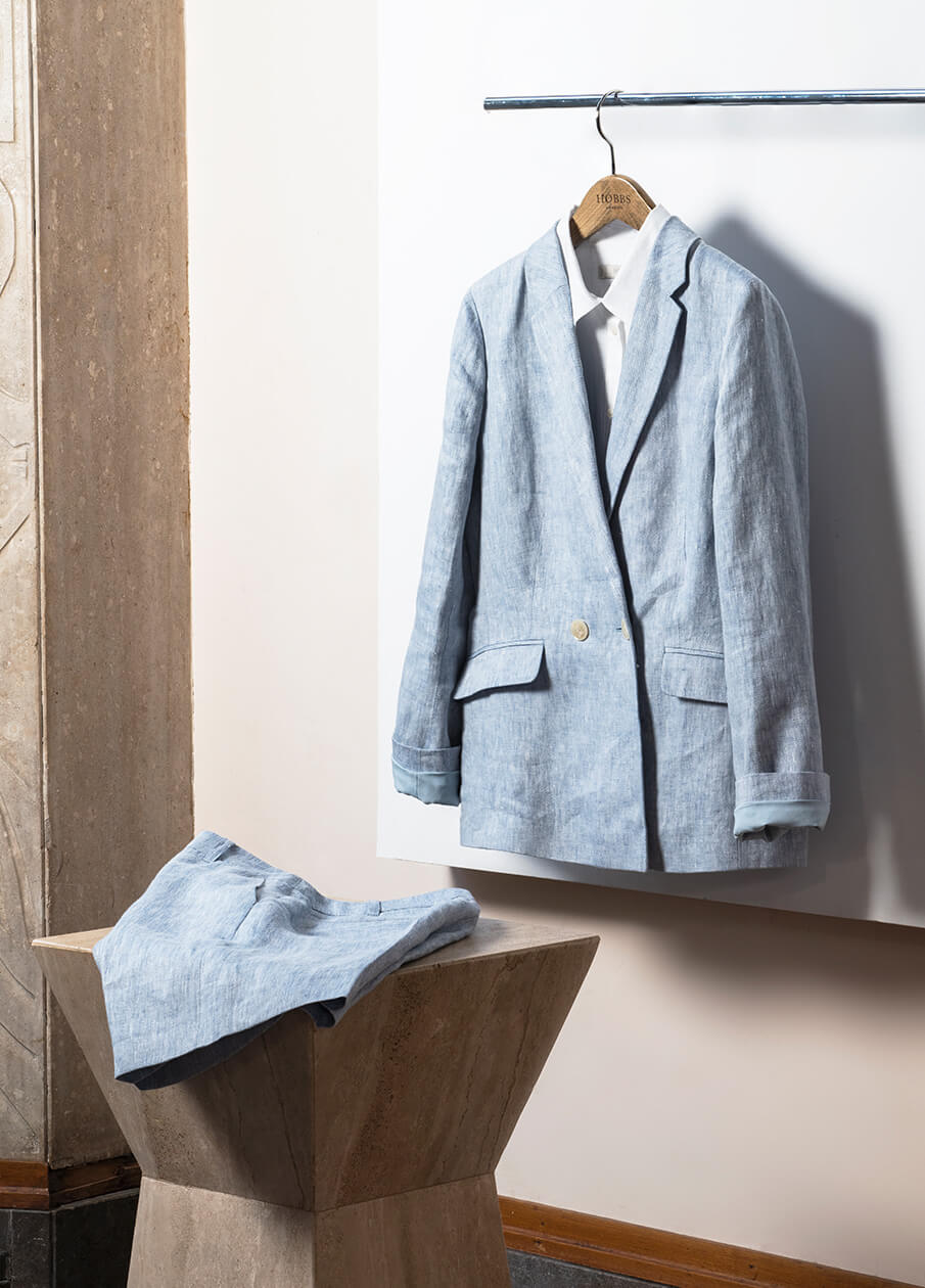 A Hobbs linen blazer hangs next to a matching pair of linen shorts sitting atop a plinth.