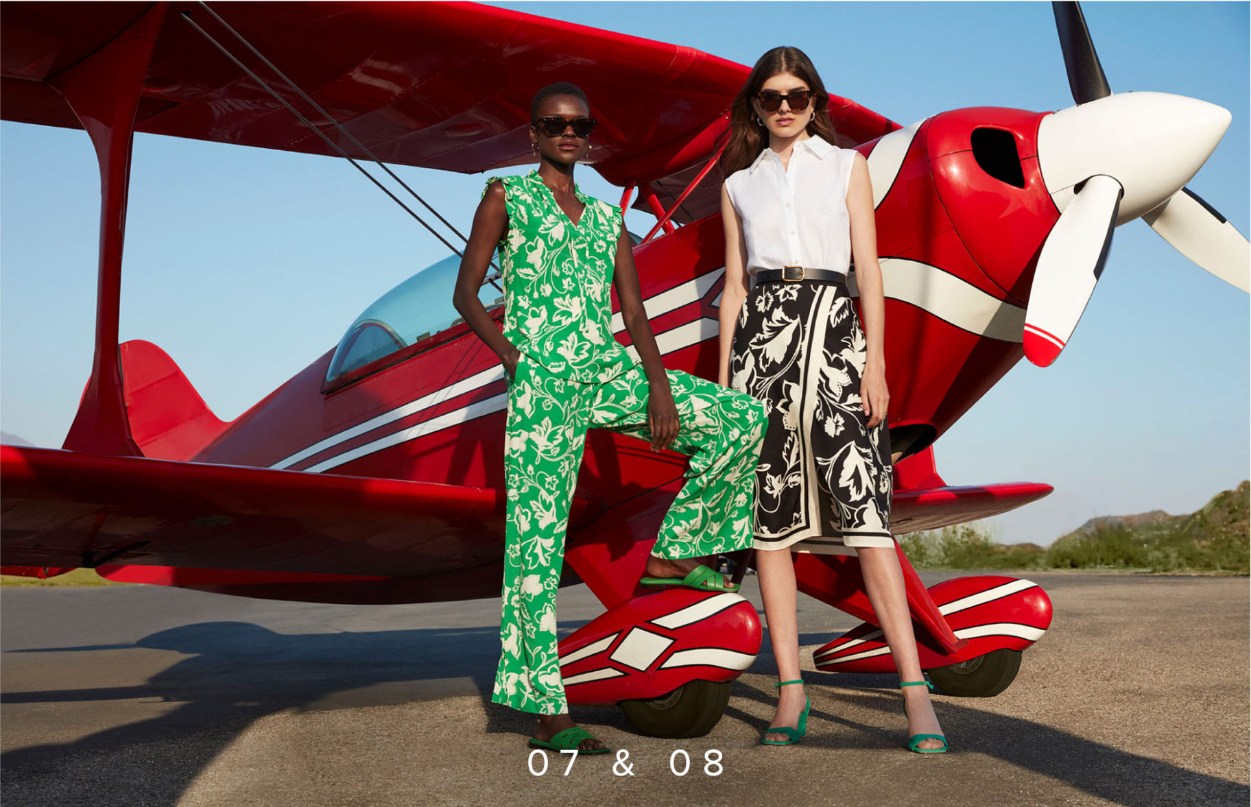 Image of two models pictured in front of an aeroplane wearing a floral print skirt and a linen shirt, floral print trousers and a floral top.
