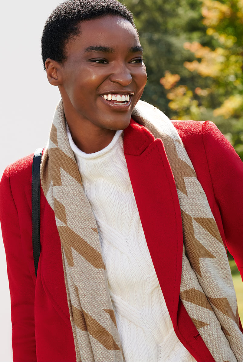 Close-up image of model wearing a Hobbs red coat, a cream jumper and a houndstooth scarf.