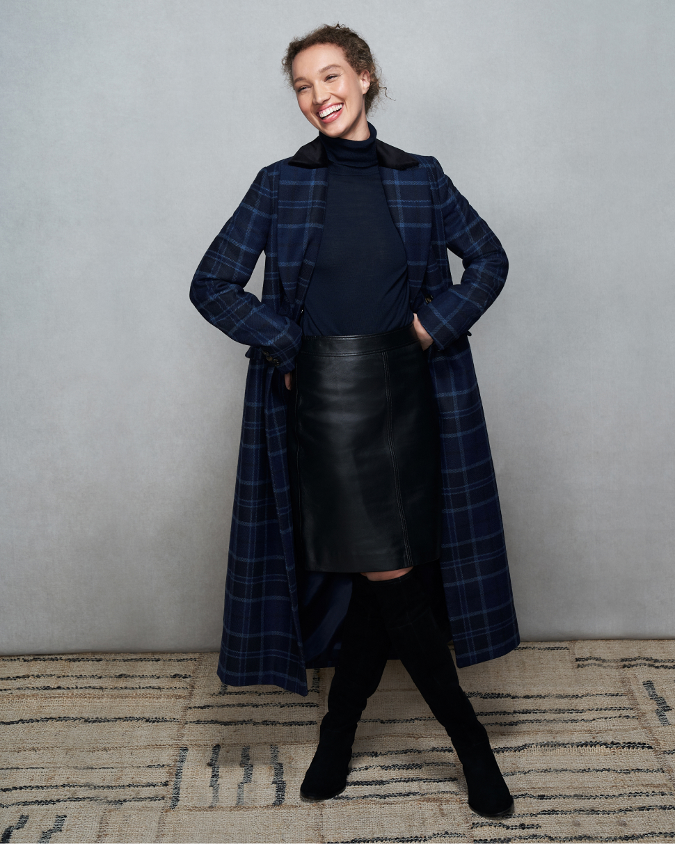 Model photographed against a canvas background wearing a Hobbs checked coat, roll neck jumper, leather skirt and over-the-knee boots.
