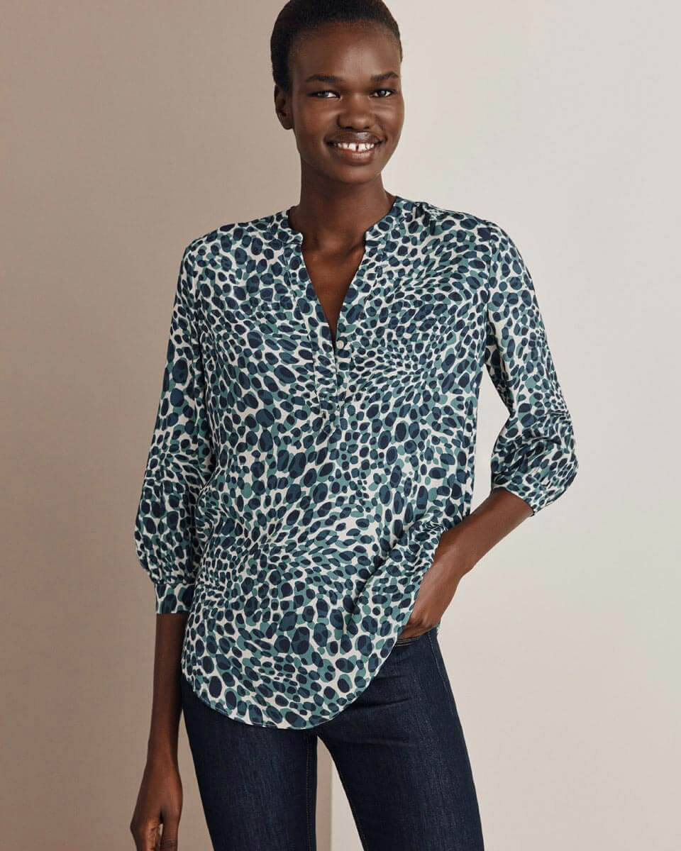 Hobbs model photographed wearing an abstract leopard print blouse with dark denim wash jeans.