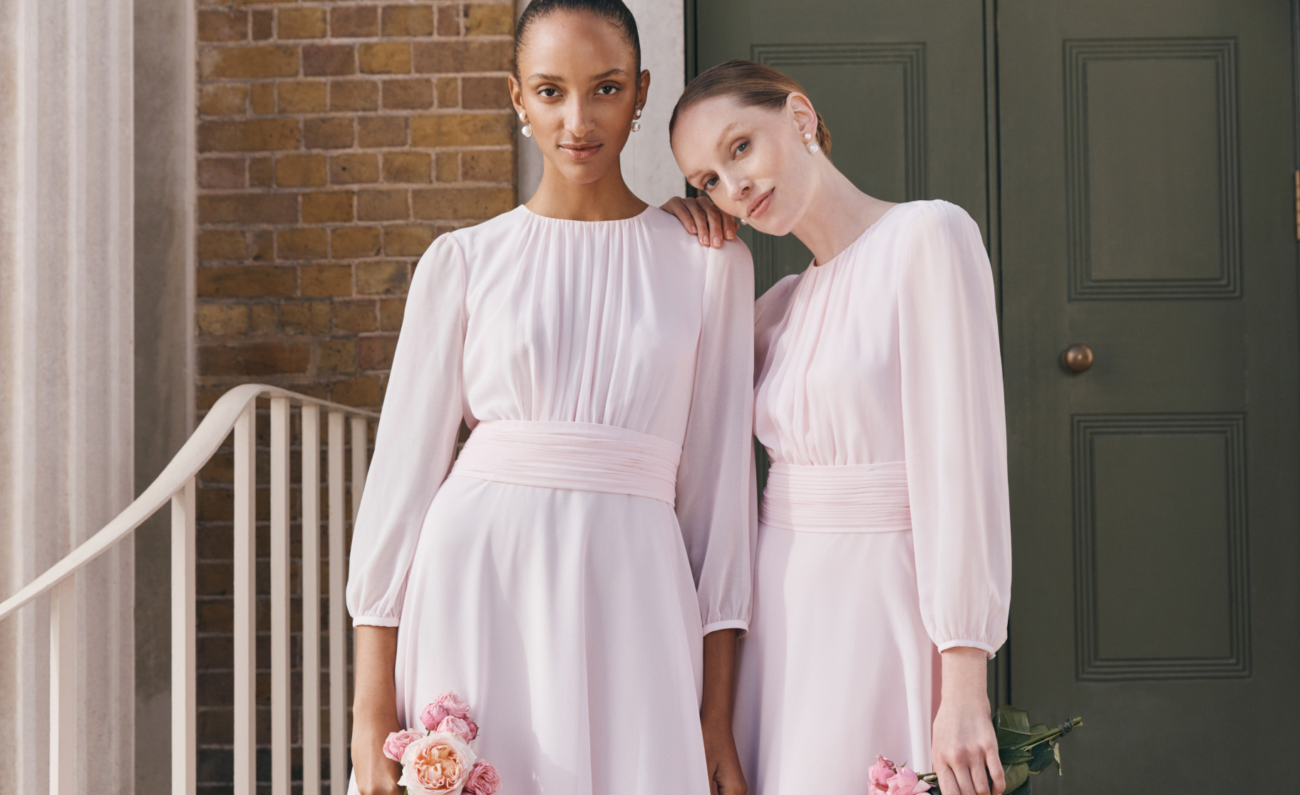 Image of two models standing in front of a wedding venue wearing bridesmaid dresses.