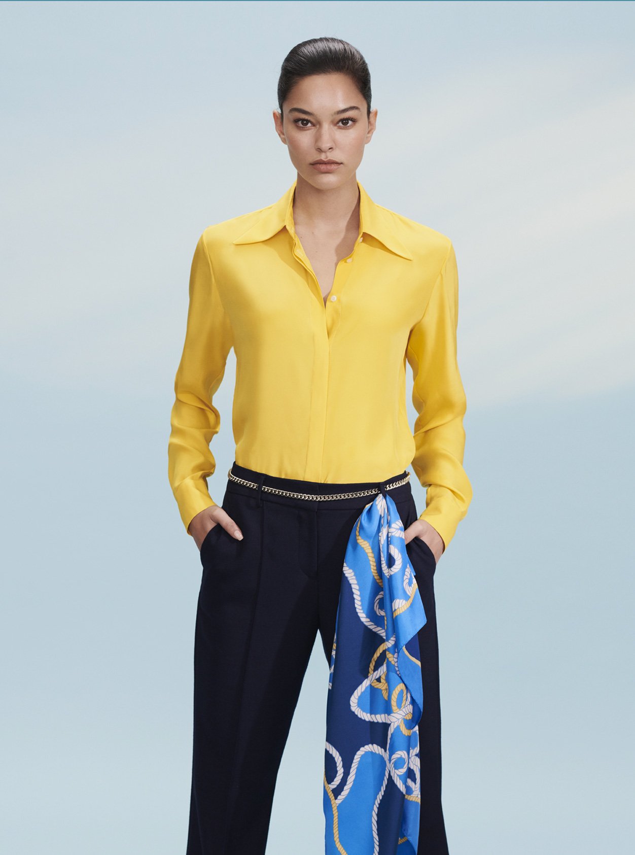 Yellow long-sleeved shirt paired with black work trousers, contrasted by a blue silk scarf draping on the waist, a stylish women’s workwear outfit by Hobbs.