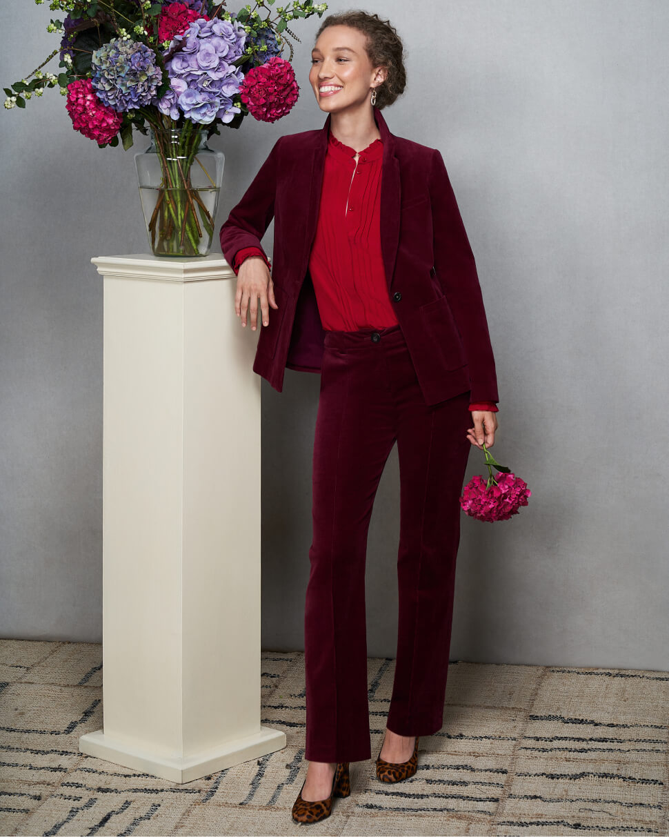 Model photographed against a canvas background wearing a Hobbs burgundy corduroy suit with a red blouse and leopard print heeled shoes.