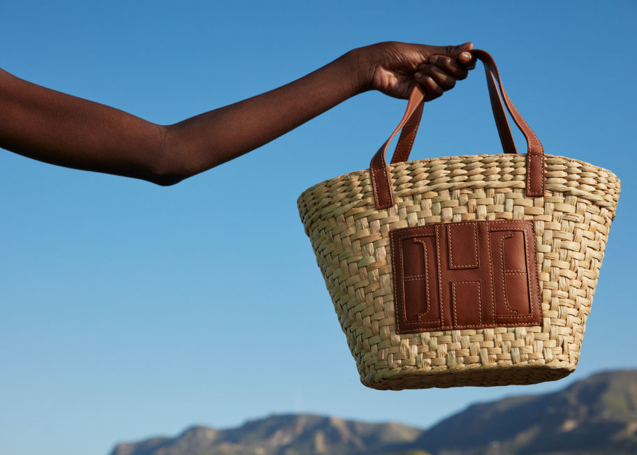 Image of a model holding a wicker bag in front of a blue sky.