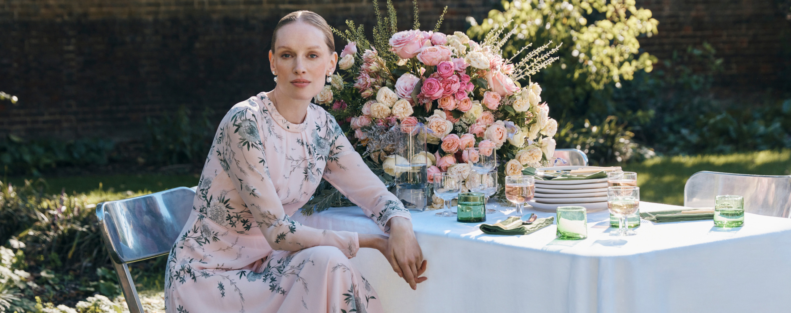 Three models pictured at a wedding around a table wearing occasion dresses.