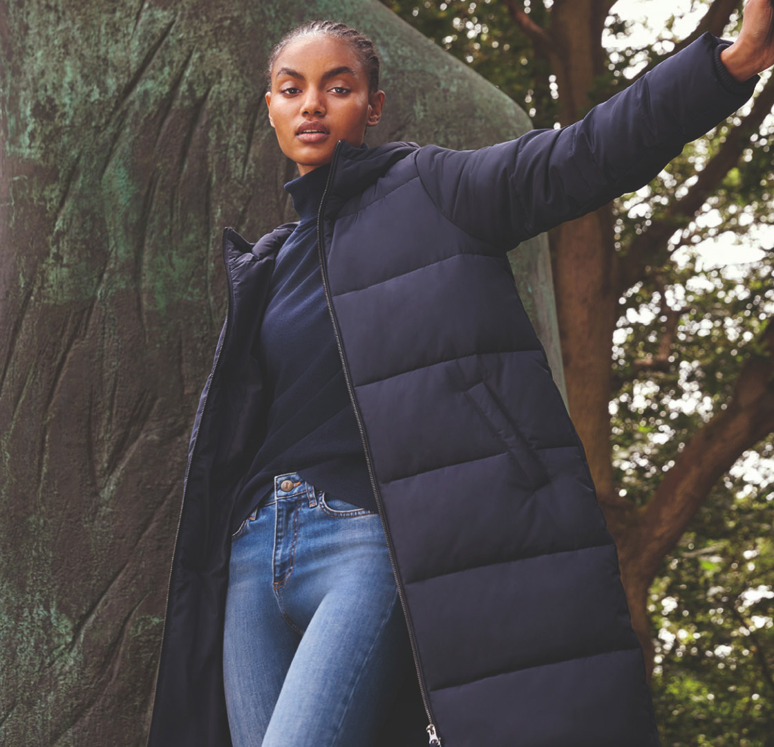 Model photographed leaning on an outdoor  sculpture in a navy puffer jacket.