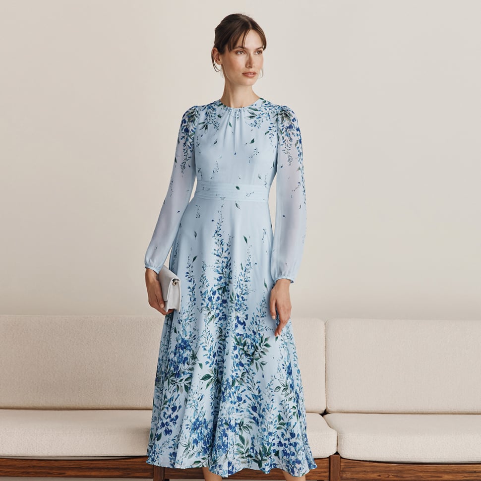 Hobbs models stand in front of a cream sofa wearing a blue floral silk midi dress.