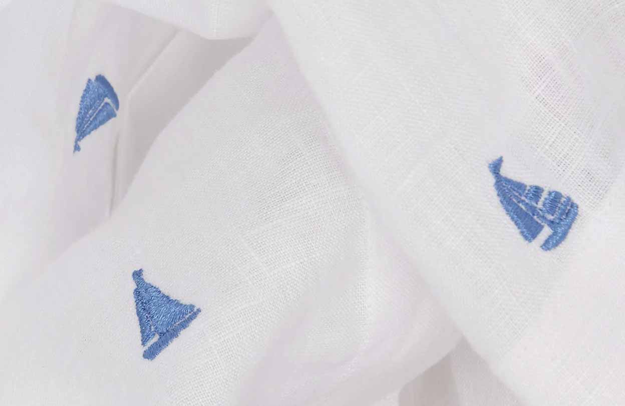 Close-up image of blue embroidered boats on white linen fabric.