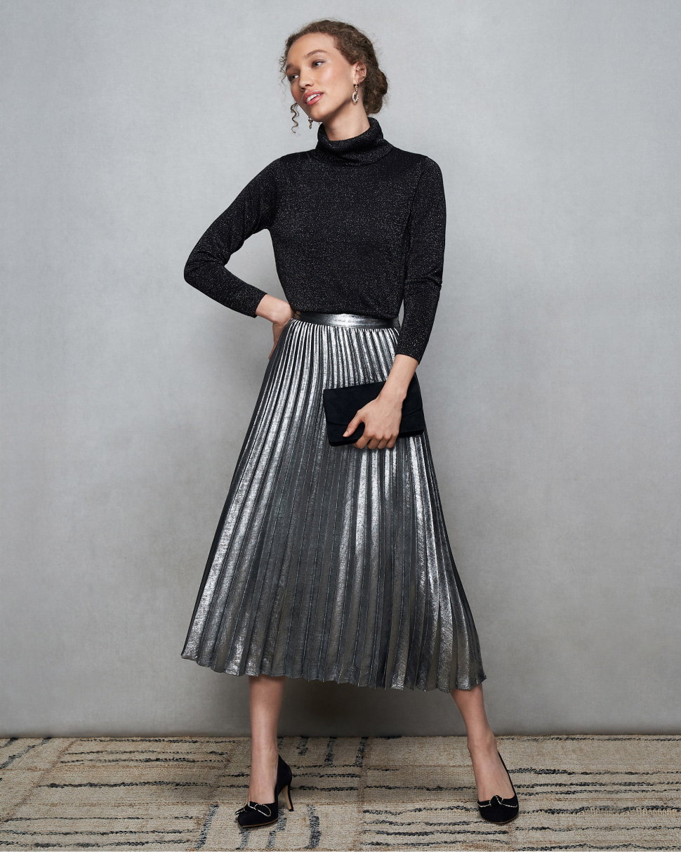 Model photographed against a canvas background wearing a Hobbs sparkle jumper and metallic pleated skirt.