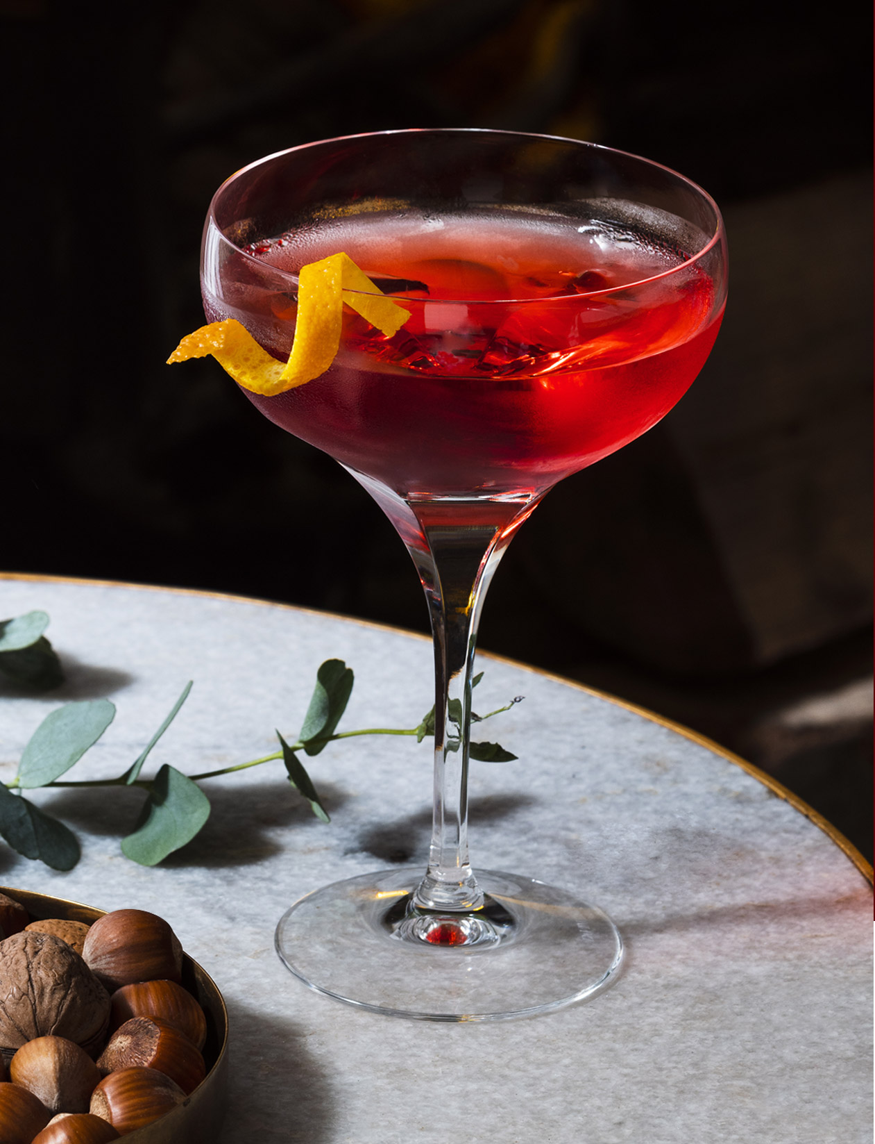 Coupe glass on marble table, filled with a festive Negroni cocktail drink