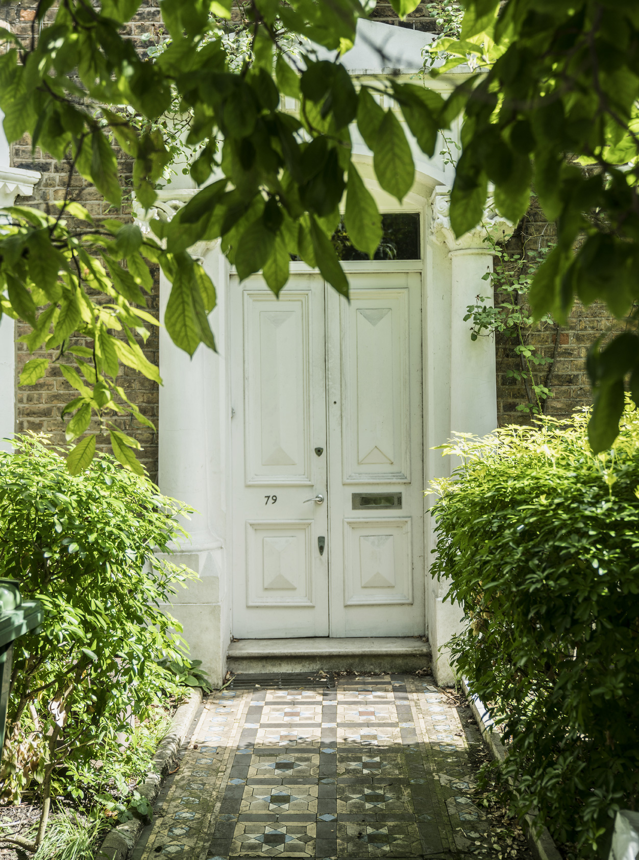 An effortlessly chic white classic London double front door with Victorian tiled path.